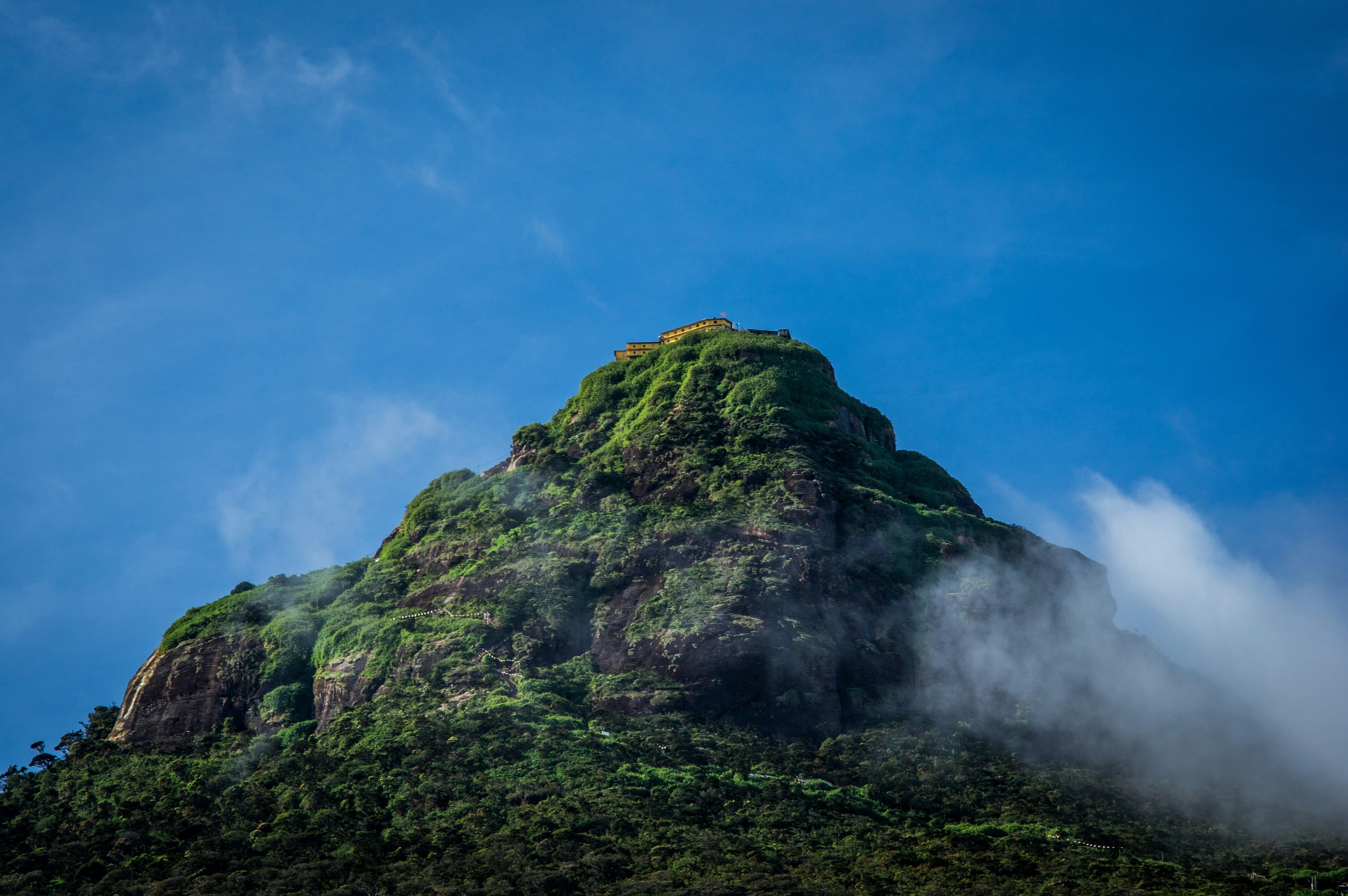 Spectacular sunrise view from Adams Peak summit showing the sacred mountains shadow and pilgrims watching the dawn