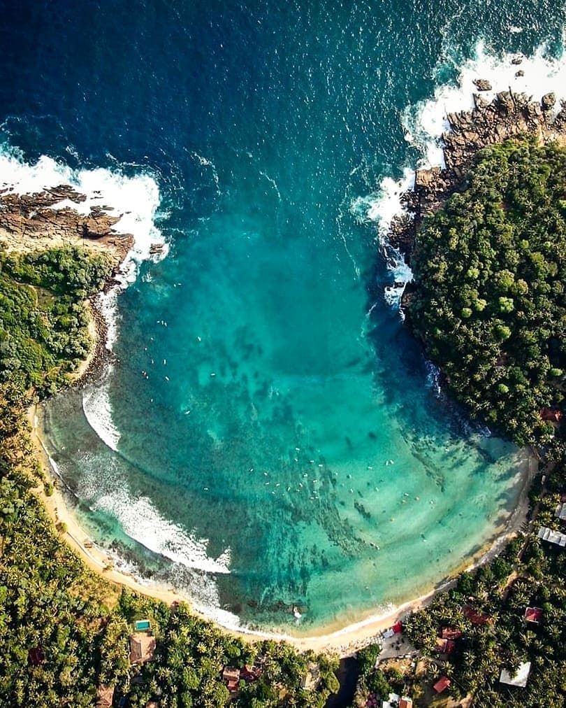 Perfect horseshoe bay of Hiriketiya Beach with surfers and coconut palms