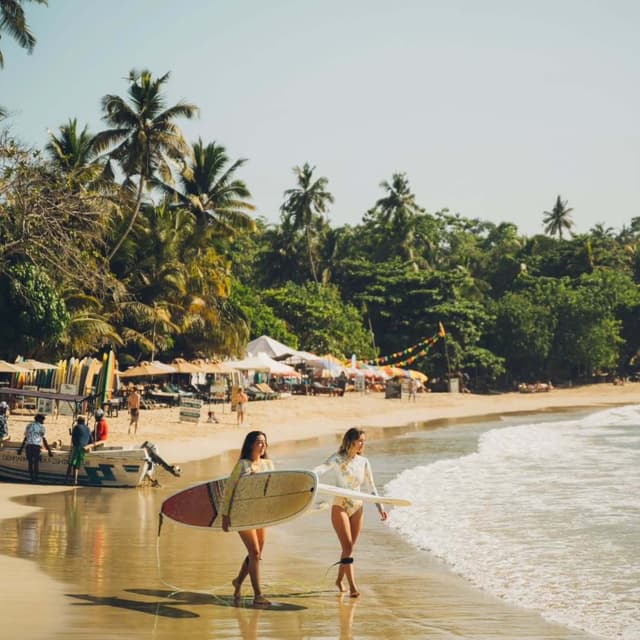 Hirikatiya Beach with surfers riding waves and palm trees lining the shore