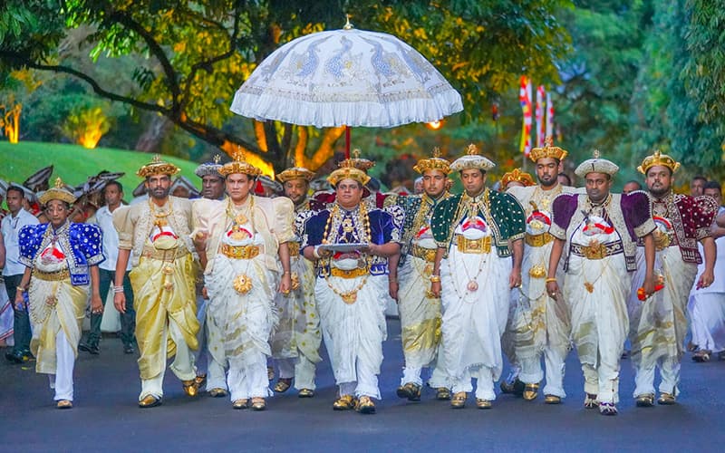 Nilame dressed in magnificent traditional Kandyan costume with tall golden hat, white silk jacket, colorful waist cloth, and golden jewelry