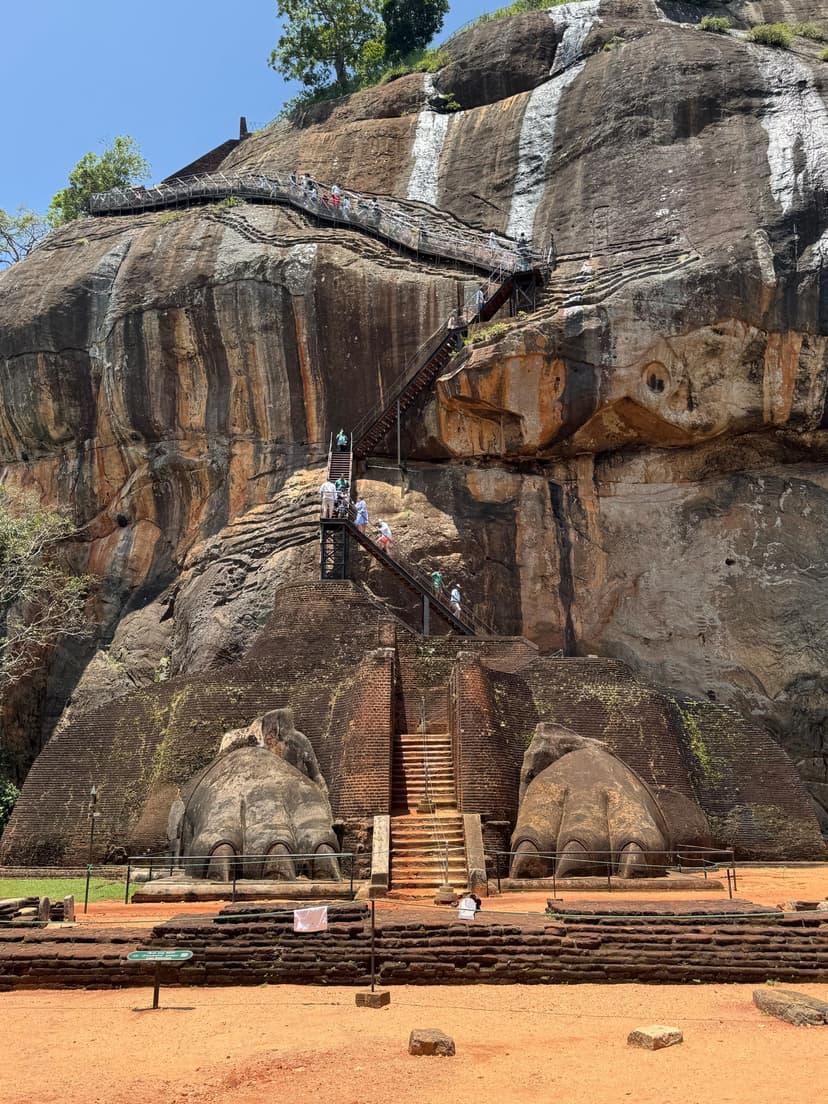 Giant stone lion paws at Sigiriya with tourists climbing metal stairs between them