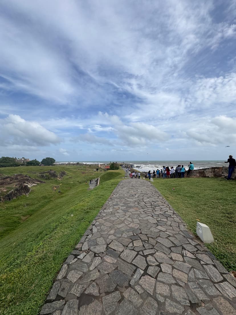 People walking along Galle Fort ramparts during golden hour with ocean views and lighthouse visible